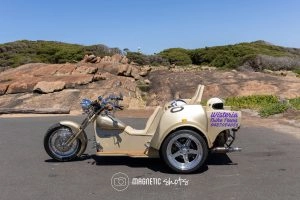 A Beige Touring Trike With A Sidecar Is Parked On A Paved Surface. A Sign On The Side Reads 