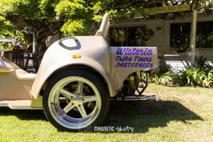 Side View Of A Beige Trike Used For Tours, Parked On Grass. A Sign On The Back Reads 