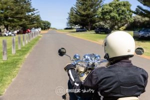 Person Wearing A Helmet Rides A Motorcycle On A Paved Road Lined With Trees And Parked Cars.